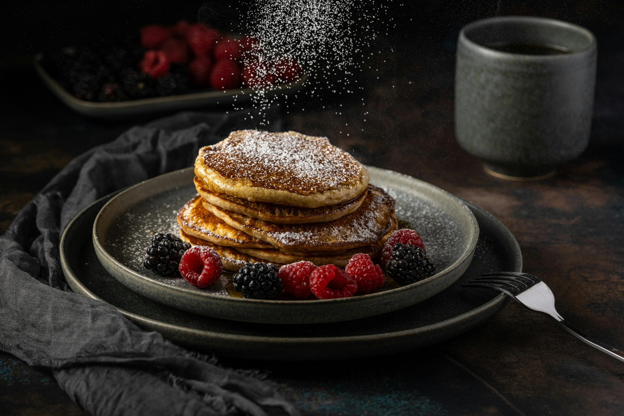 Stacked pancakes with berries and powdered sugar create a cozy breakfast scene.